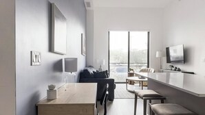 Un saló modern i minimalista amb un finestral gran, una televisió de pantalla plana i una zona de menjador amb una taula i cadires de fusta.