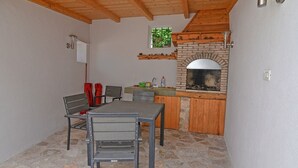 A dining area with a stone fireplace, a wooden ceiling, and a window with a view of greenery. - Mariana / Mariana A3 (Veli Lošinj)