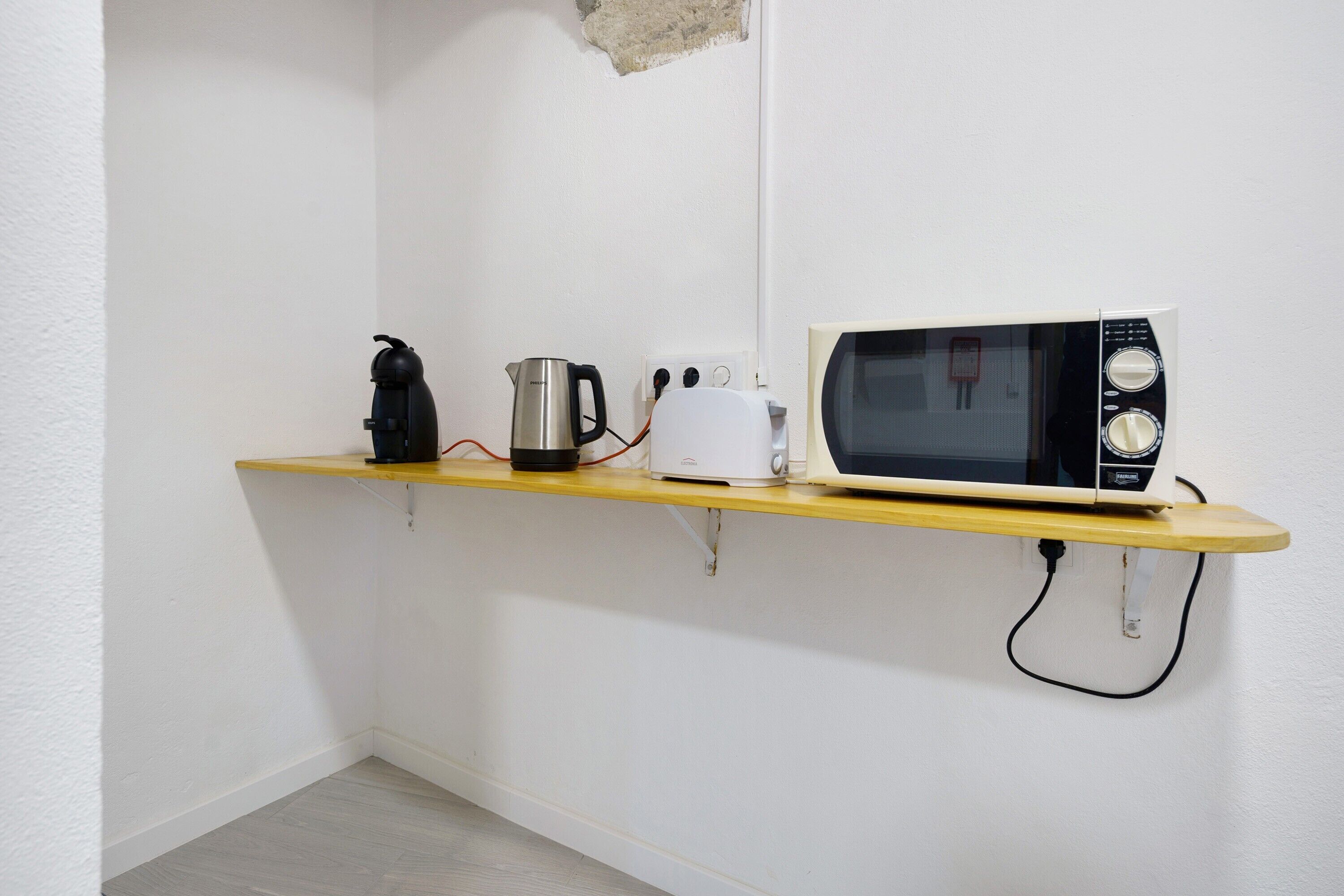 Une cuisine équipée d’un four à micro-ondes, d’un grille-pain et d’une bouilloire, le tout posé sur une étagère en bois.