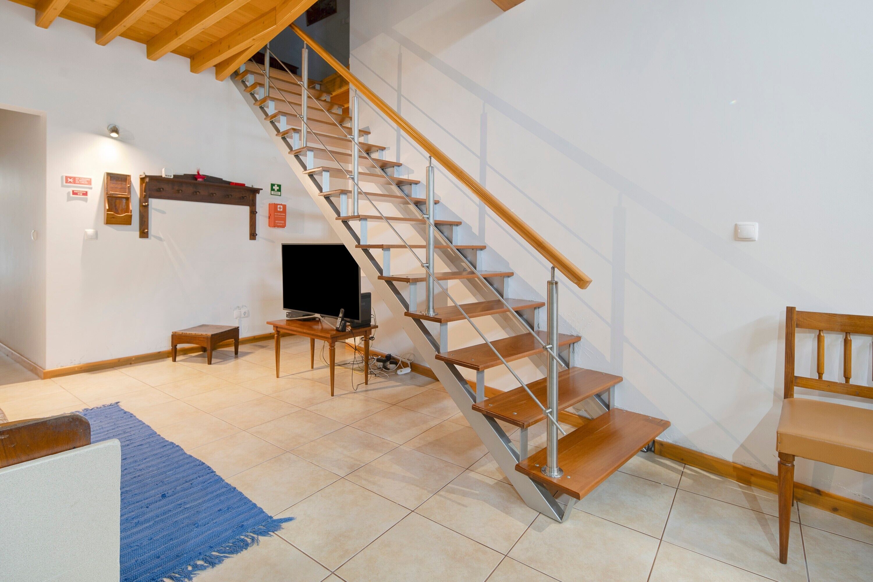 A staircase with wooden steps and metal railings, a television on a stand, a small table, and a blue rug on the floor.