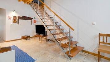 A staircase with wooden steps and metal railings, a television on a stand, a small table, and a blue rug on the floor.