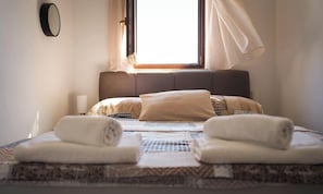 A neatly made bed with a patterned bedspread, two rolled towels, a bedside lamp, and a window with curtains. - Castello / Castello A3 (Mali Lošinj)