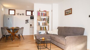 Una sala de estar con un sofá gris, una mesa de comedor con sillas, una estantería y una pequeña mesa con una vela.