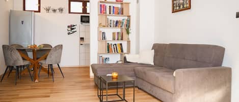 Un salon avec un canapé gris, une table à manger avec des chaises, une bibliothèque et une petite table sur laquelle est posée une bougie.