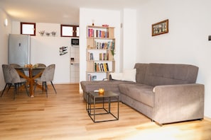 A living room with a grey sofa, a dining table with chairs, a bookshelf, and a small table with a candle. - Castello / Castello A3 (Mali Lošinj)