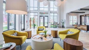A spacious lobby with large windows, yellow armchairs, a central coffee table, and a reception desk. - Landing | Amazing 1BD, Clubhouse, Pool (Charlotte)