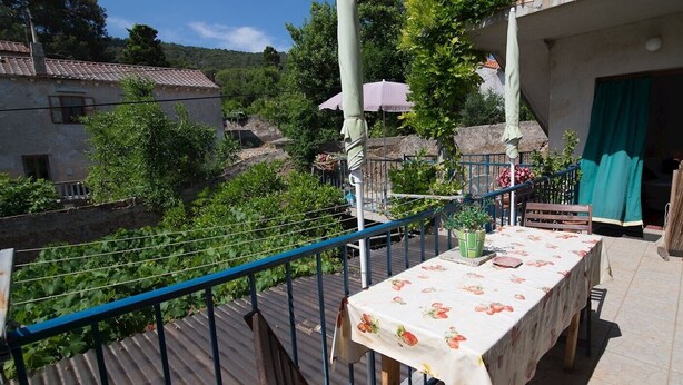 Een balkon met een eettafel, omgeven door groen en uitzicht op een dorp.