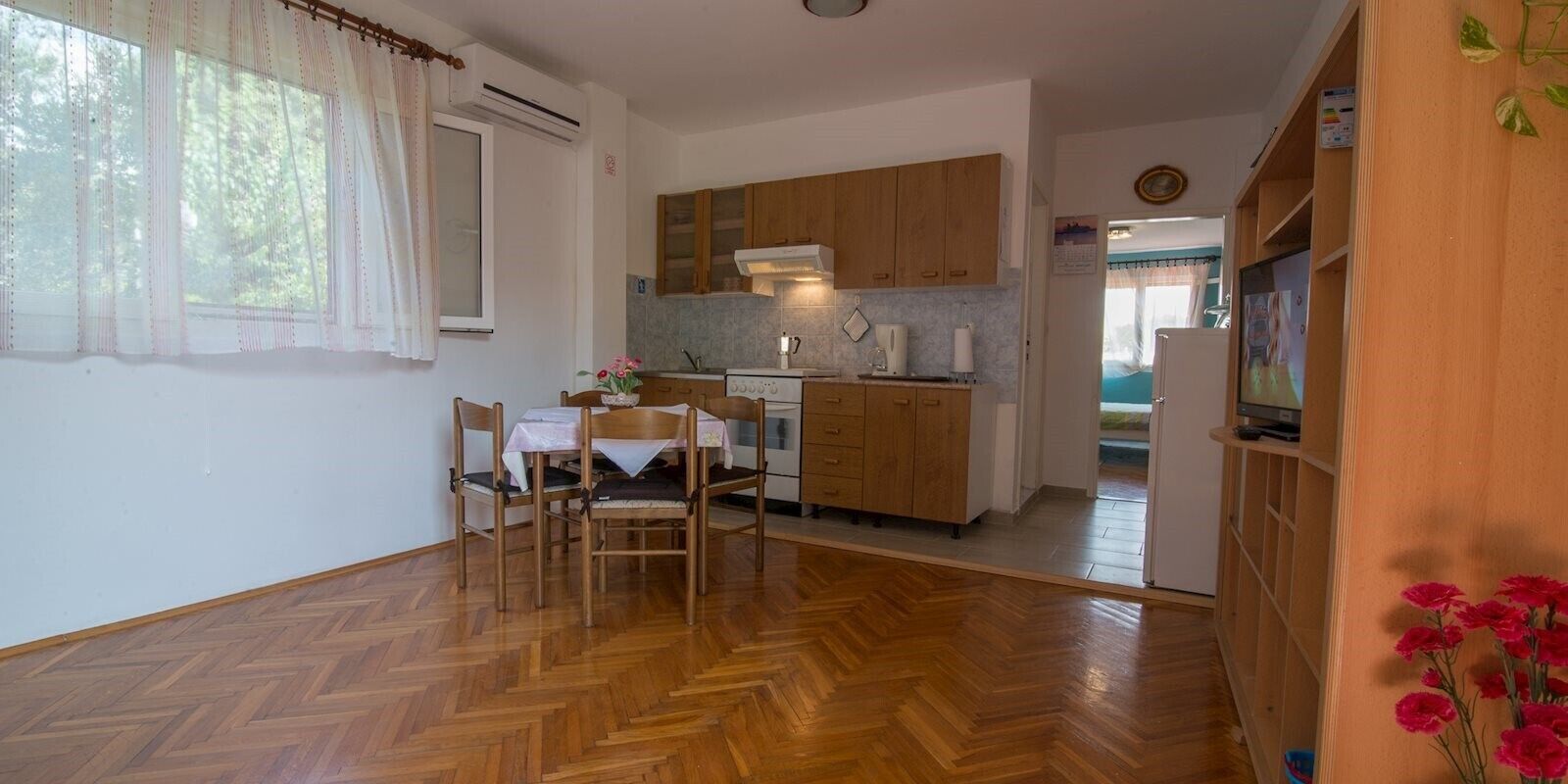 Cozinha compacta com armários de madeira, área de jantar com mesa e cadeiras, e vista para um quarto.