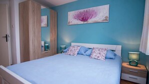 Een slaapkamer met een bed, nachtkastje, spiegel en een aan de muur hangend schilderij.