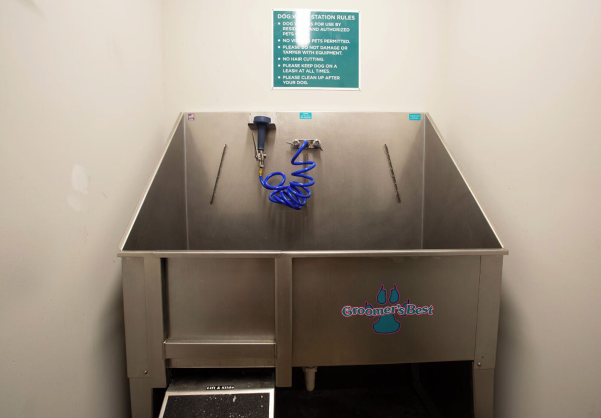 A metal sink with a hose and a dog leash, a sign with dog station rules, and a logo on the sink.
