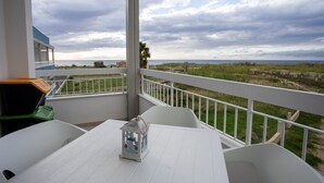 A balcony with a white table and chairs, a decorative lantern, and a view of the sea and dunes. - Stromboli Sunset with shared pool (Villaggio del Golfo)