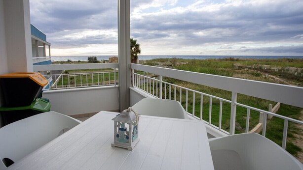 A balcony with a white table and chairs, a decorative lantern, and a view of the sea and dunes. - Stromboli Sunset with shared pool (Villaggio del Golfo)