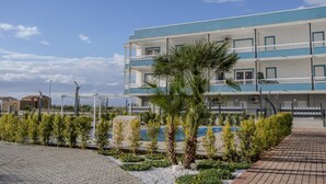 A multi-story hotel with balconies, a paved walkway, and a landscaped garden with palm trees. - Stromboli Sunset with shared pool (Villaggio del Golfo)