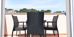Un balcón con dos sillas de mimbre y una mesa, con vistas a un barrio residencial con casas y árboles.