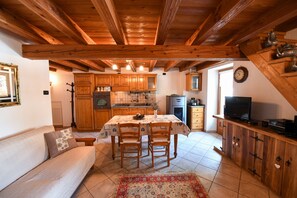 A cozy kitchen with wooden beams, a dining table, chairs, and a TV on a wooden cabinet.
