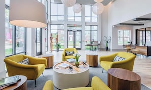 A spacious lobby with large windows, yellow armchairs, a central coffee table, and a reception desk. - Landing | Modern Studio, Gym, Clubhouse (Charlotte)