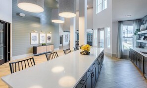 A modern kitchen with a large island, pendant lighting, and a view to the outside. - Landing | Modern Studio, Gym, Clubhouse (Charlotte)