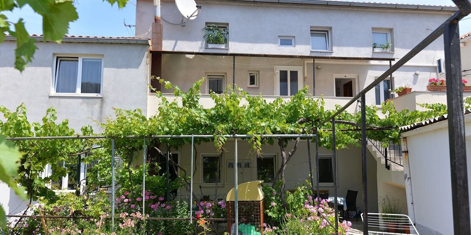 A residential building with a balcony, a satellite dish, and a small garden with flowering plants.