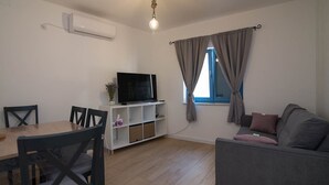 A living room with a TV, sofa, dining table, chairs, and a window with curtains. - Pinea / Pinea A2 in Veli Lošinj (Veli Lošinj)