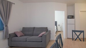 A small living area with a grey sofa, a dining table, and a kitchen area with a microwave and refrigerator. - Pinea / Pinea A2 in Veli Lošinj (Veli Lošinj)