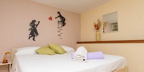 A neatly made bed with pillows, a rolled towel, and a pair of shoes on the bed. There is a wall decoration with a silhouette of a person and a heart. - Livia / Livia 3 - apartman za 2 osobe · Livia (Veli Lošinj)