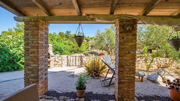Ein überdachter Patio-Bereich mit Backsteinpfeilern, hängenden Körben, einer Steinmauer und einem Stuhl.