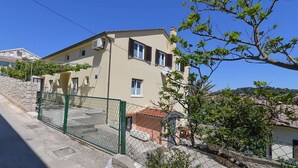 A two-story building with a beige facade, a green metal fence, and a stone wall. - Frantin / Frantin B4 (Mali Lošinj)