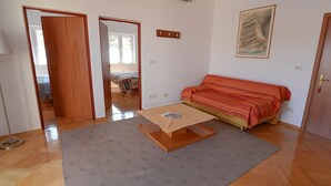 A room with a sofa, a small table, a patterned rug, and a door leading to another room. - Frantin / Frantin B4 (Mali Lošinj)