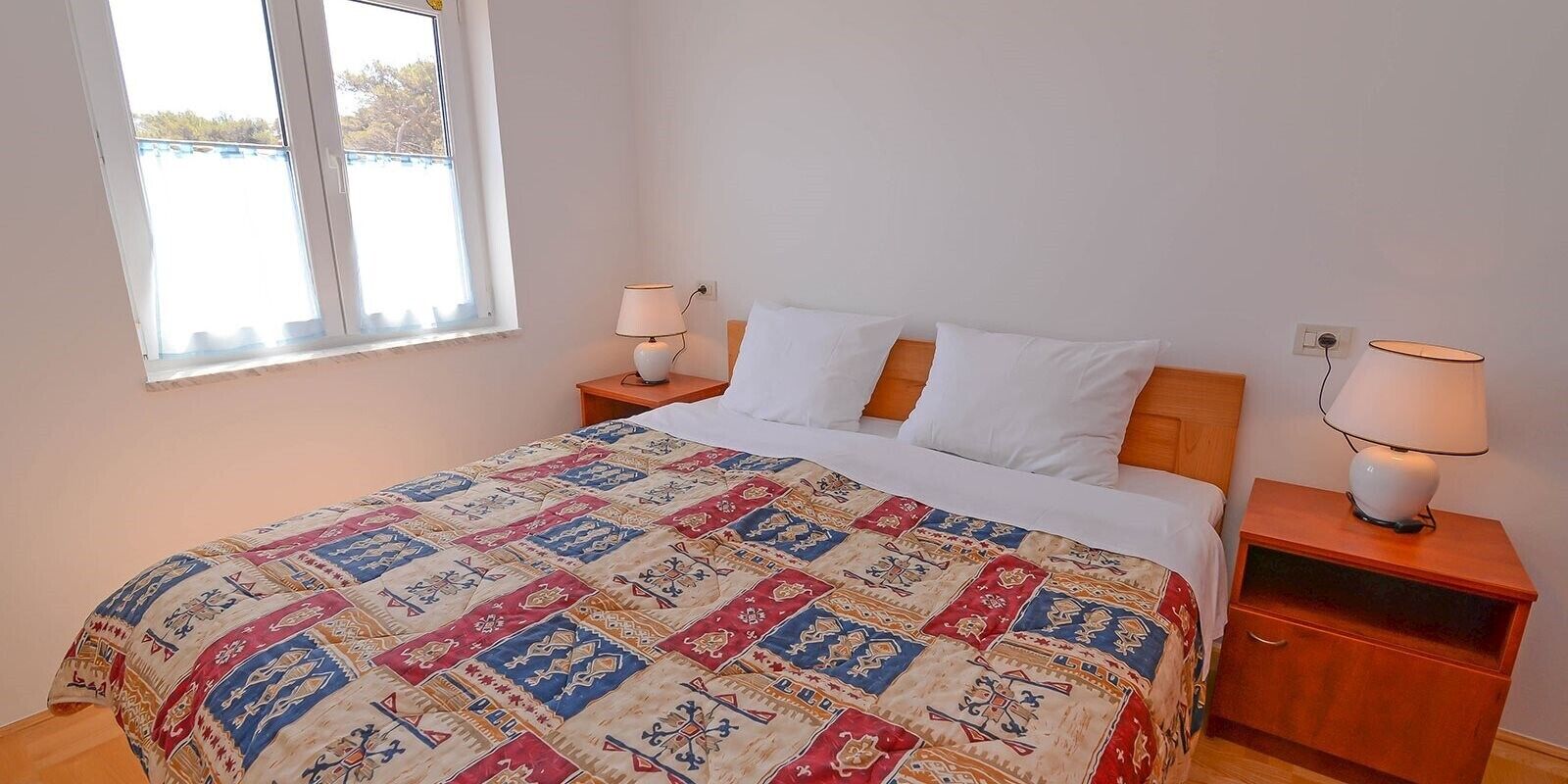 A bedroom with a bed, two bedside tables, two lamps, and a window with blinds.