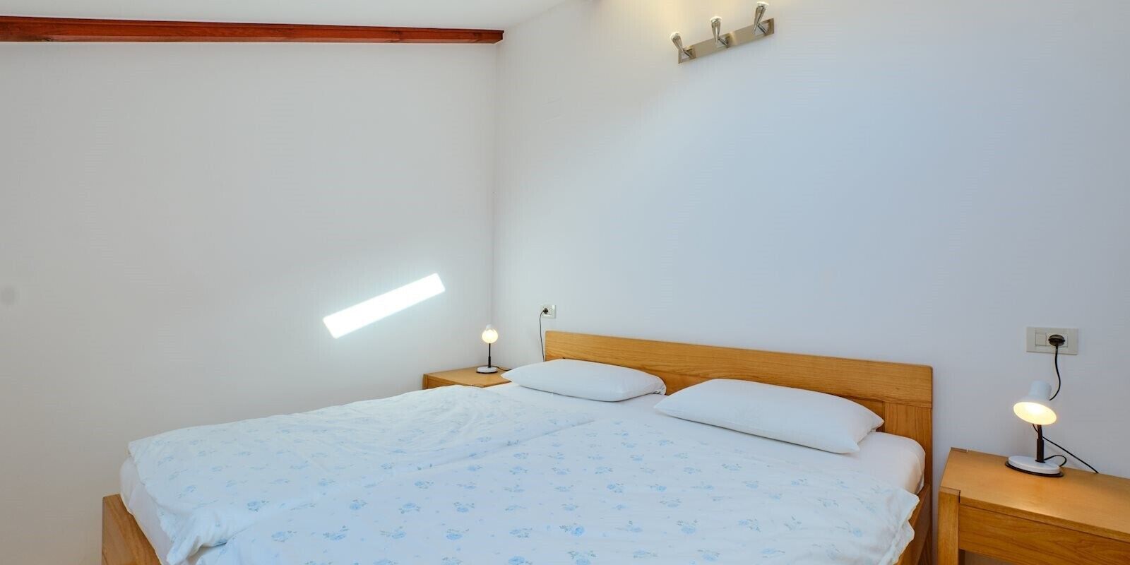 Una camera da letto con una testiera in legno, due comodini con lampade e una finestra che lascia entrare luce naturale.