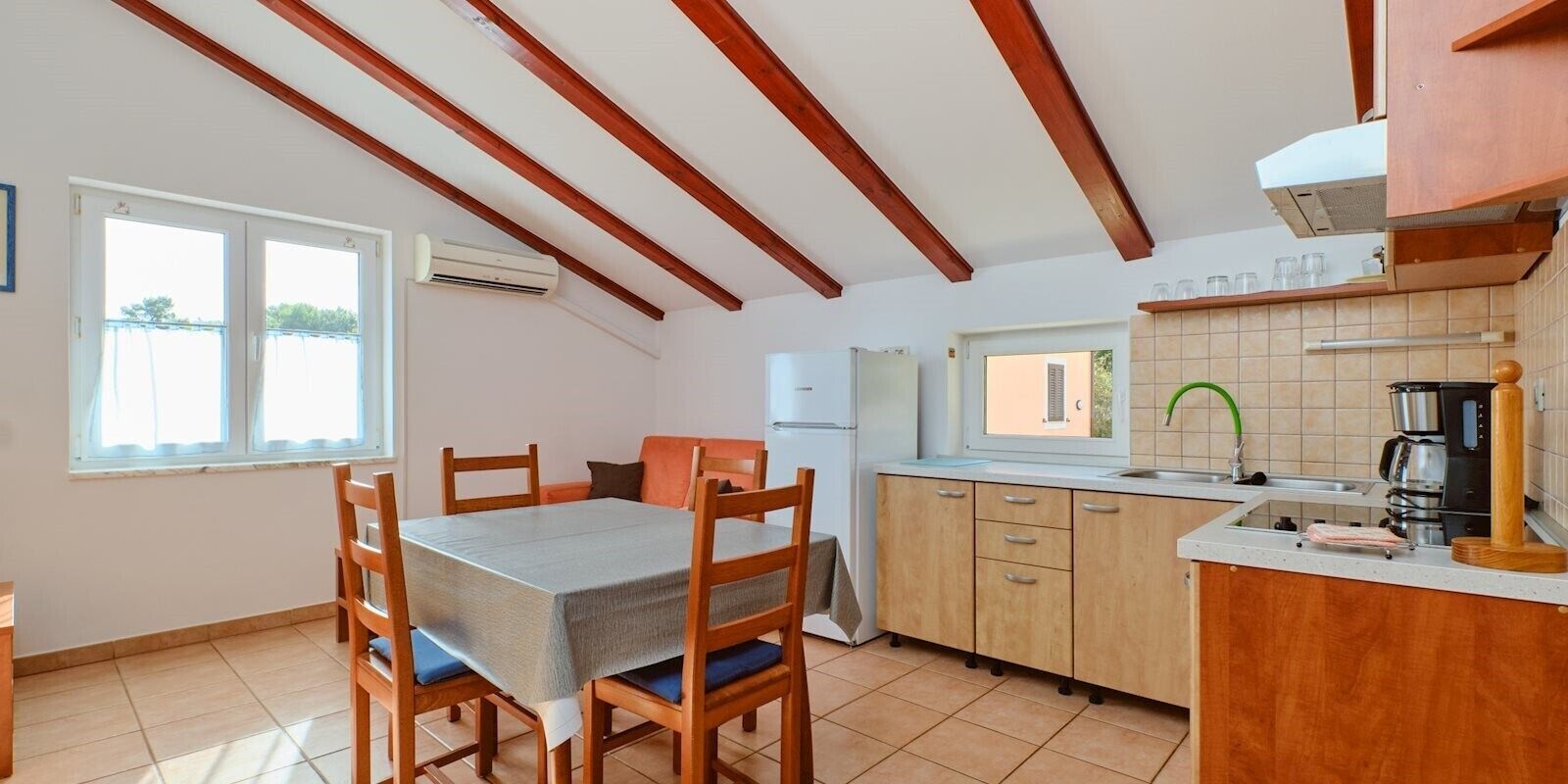 A compact kitchen with wooden cabinets, a dining table with chairs, and a window providing natural light.
