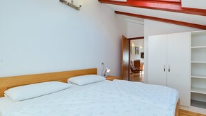 Une chambre à coucher avec une tête de lit en bois, un lit avec une literie blanche, une lampe de chevet et une armoire avec plusieurs étagères.