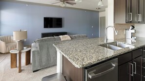 Cozinha moderna com bancadas de granito, eletrodomésticos de aço inoxidável e armários escuros.