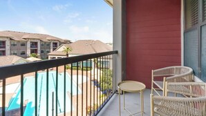 A balcony with a view of a swimming pool, wicker chairs, and a small table. - Landing | Modern 1BD, Pool, Gym (Houston)