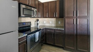A kitchen with dark brown cabinets, a stainless steel refrigerator, a microwave, a stove, and a tiled backsplash. - Landing | Modern 1BD, Pool, Gym (Houston)