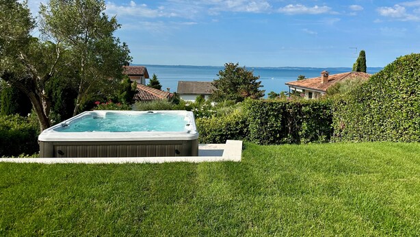 A hot tub in a lush garden with a view of the sea and houses in the background. - Villa Venezia Garda: Lake View, Garden & Jacuzzi (Garda)