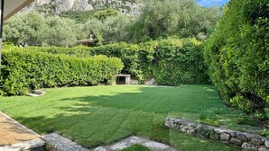 A well-maintained garden with a stone pathway, neatly trimmed hedges, and a mountain backdrop. - Villa Venezia Garda: Lake View, Garden & Jacuzzi (Garda)