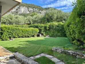 Un giardino curato con un sentiero in pietra, siepi ben potate e montagne sullo sfondo.
