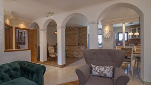 Un salón espacioso con un sofá de terciopelo verde, un sillón gris y un comedor con una pared de acento de piedra.