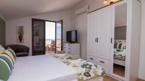 Un dormitorio con cama, televisor, armario, silla y balcón con vistas.