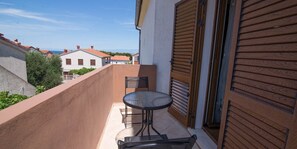 Un balcón con mesa y sillas, una puerta de madera y vistas a edificios al fondo.