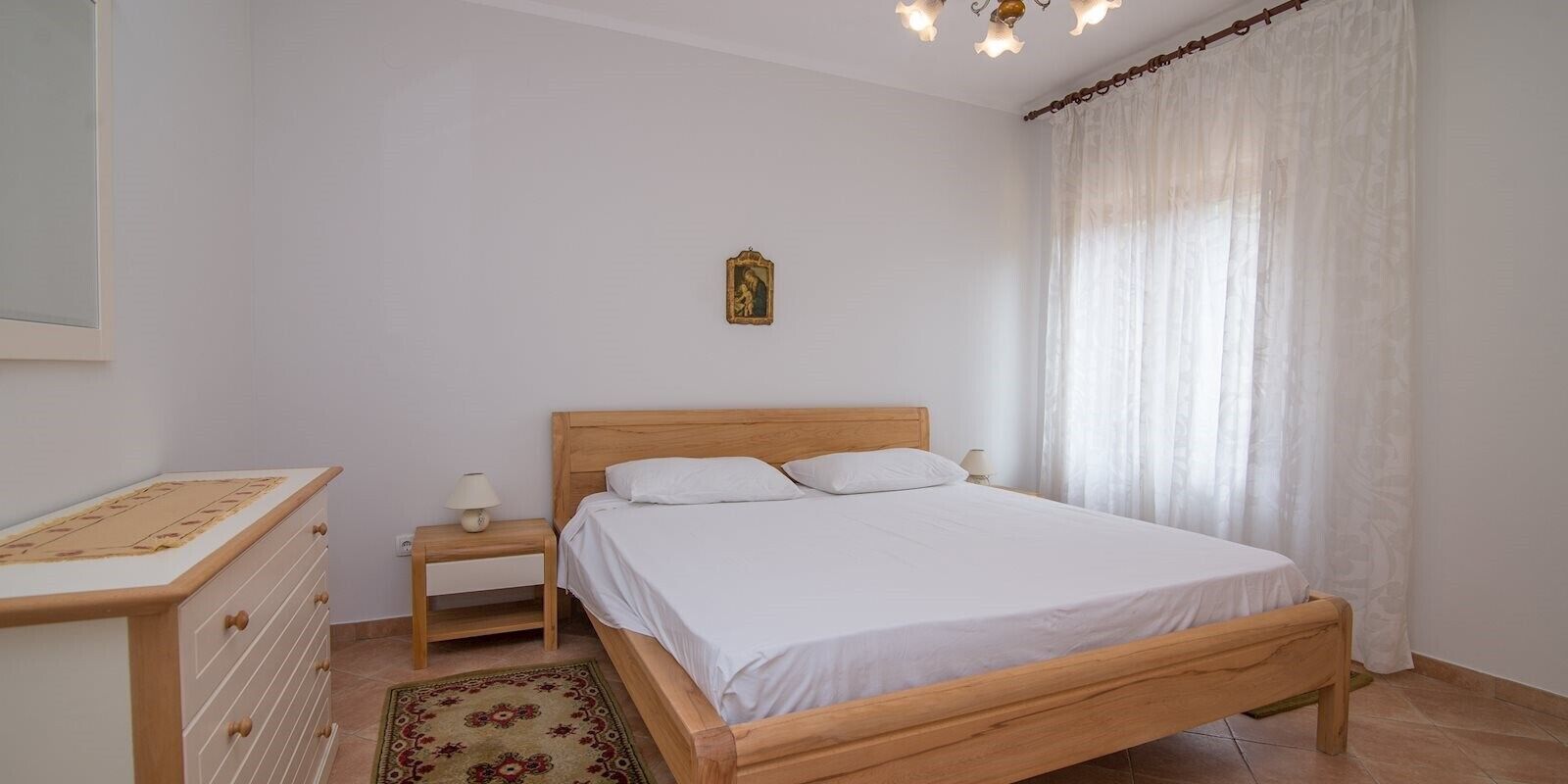 Ein Schlafzimmer mit einem hölzernen Bett, einem Nachttisch, einer Kommode und einem kleinen Tisch mit einer Lampe.