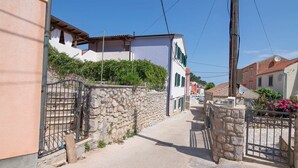 A narrow street with stone walls and traditional buildings, featuring a gated entrance and a clear sky. - Ivana C6 in Veli Lošinj (Veli Lošinj)