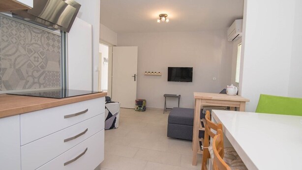 A modern kitchen with white cabinets, a wooden countertop, and a built-in stove. There is a dining area with a white table and chairs, and a TV mounted on the wall. - Ivana C6 in Veli Lošinj (Veli Lošinj)