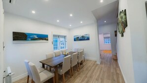 A dining area with a wooden table and chairs, a window with white shutters, and two wall-mounted paintings. - Holiday Home 'Douro Garden Home Rooftop' with Private Terrace, Wi-Fi and Air Conditioning (Vila Nova de Gaia)