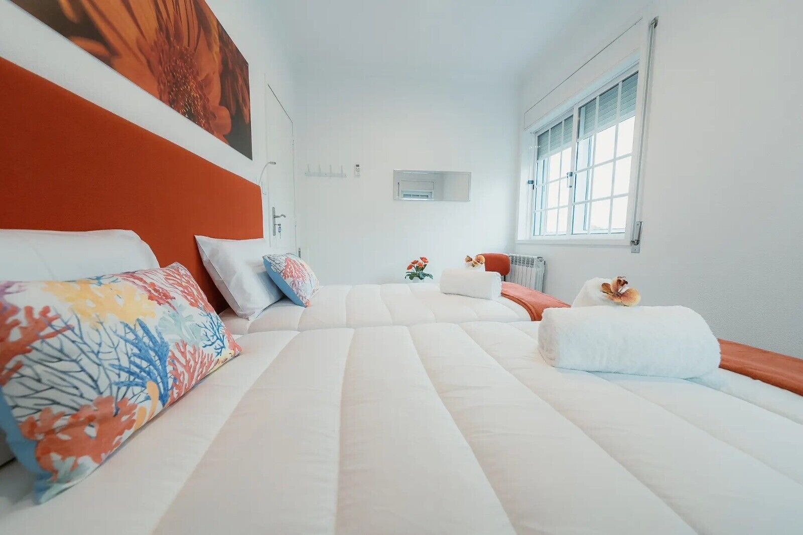 A hotel room with a bed, pillows, a window, and a radiator.