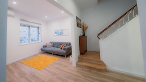A spacious living area with a sofa, a wooden staircase, and a window with a view. - Holiday Home 'Douro Garden Home Rooftop' with Private Terrace, Wi-Fi and Air Conditioning (Vila Nova de Gaia)