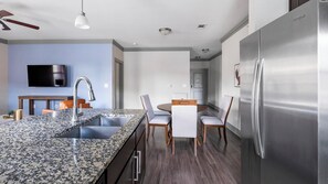 A modern kitchen with granite countertops, stainless steel appliances, and a dining area with wooden chairs and a white table. - Landing | Chic 2BD, Gym, Pool (Houston)