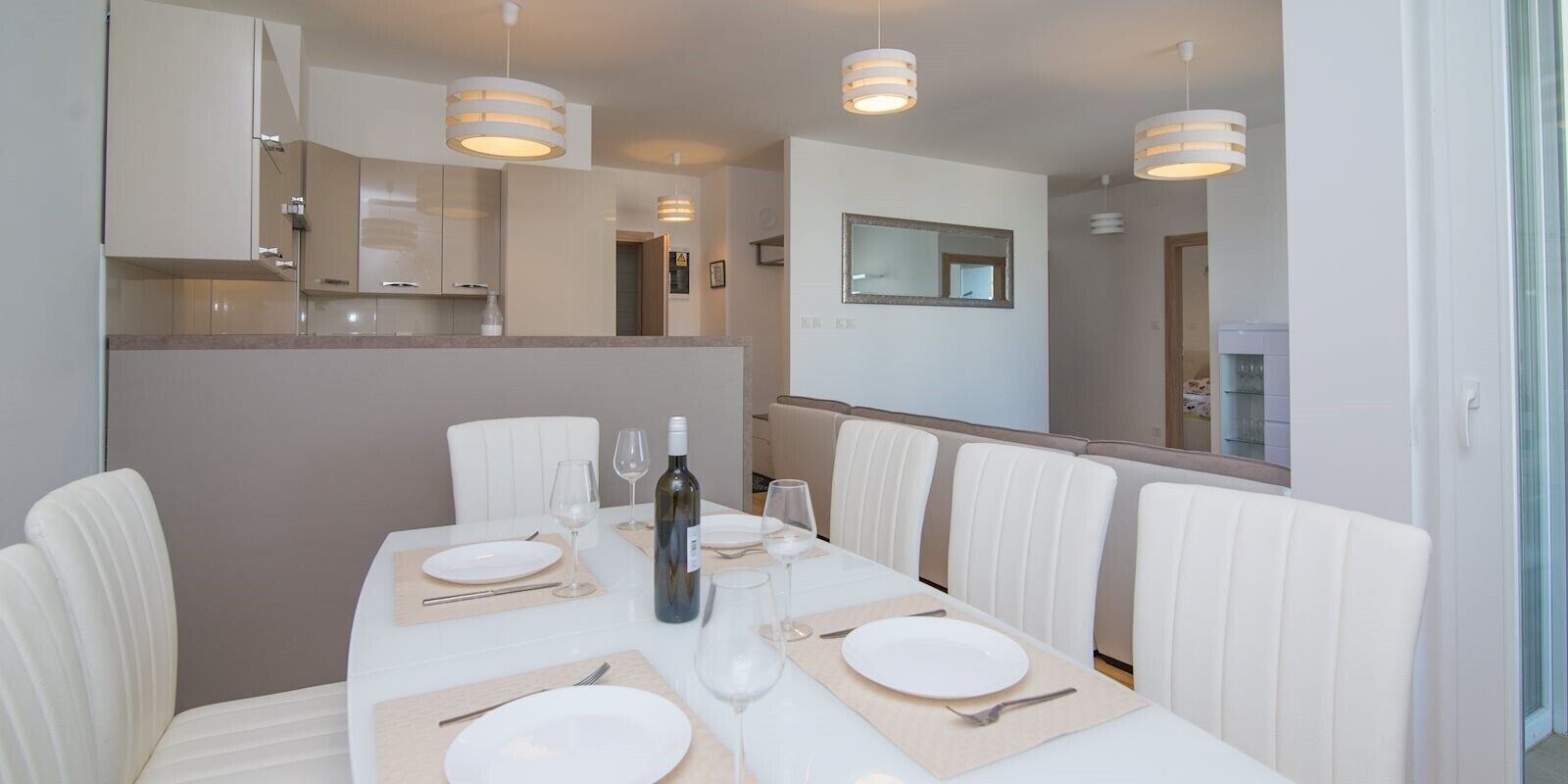 Un espace repas avec une longue table dressée pour quatre personnes, des chaises blanches et des luminaires suspendus.