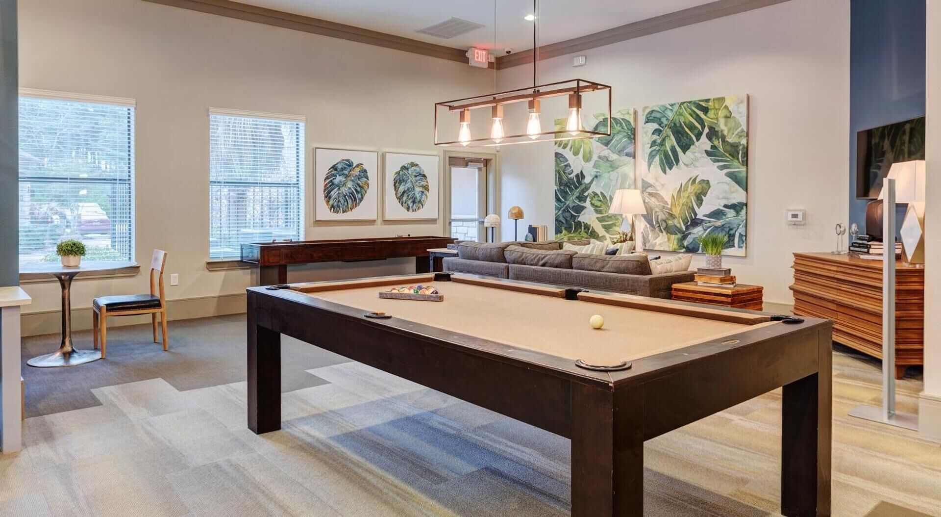 A modern living room with a pool table, a sofa, and a large window with blinds.
